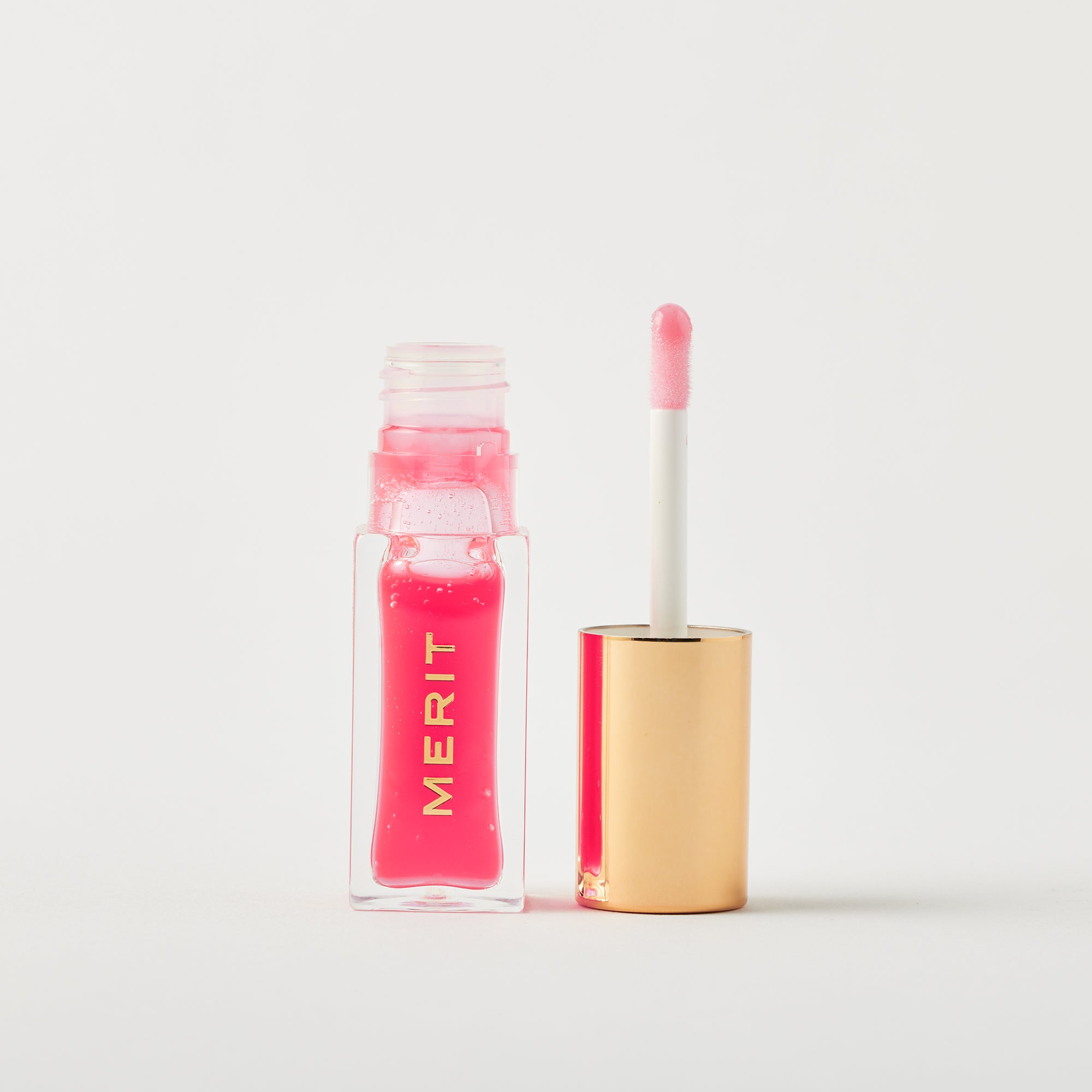 Master || A bottle of Merit lip oil in shade Les Deux displayed next to its applicator. 