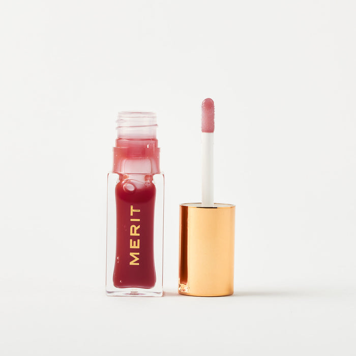 Master ||A bottle of Merit lip oil in shade Mapleton displayed next to its applicator. 