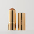 Master ||  A stick bronzer product by MERIT, with the cap off, showing the bronzing cream inside and MERIT on the cap. Shade Clay