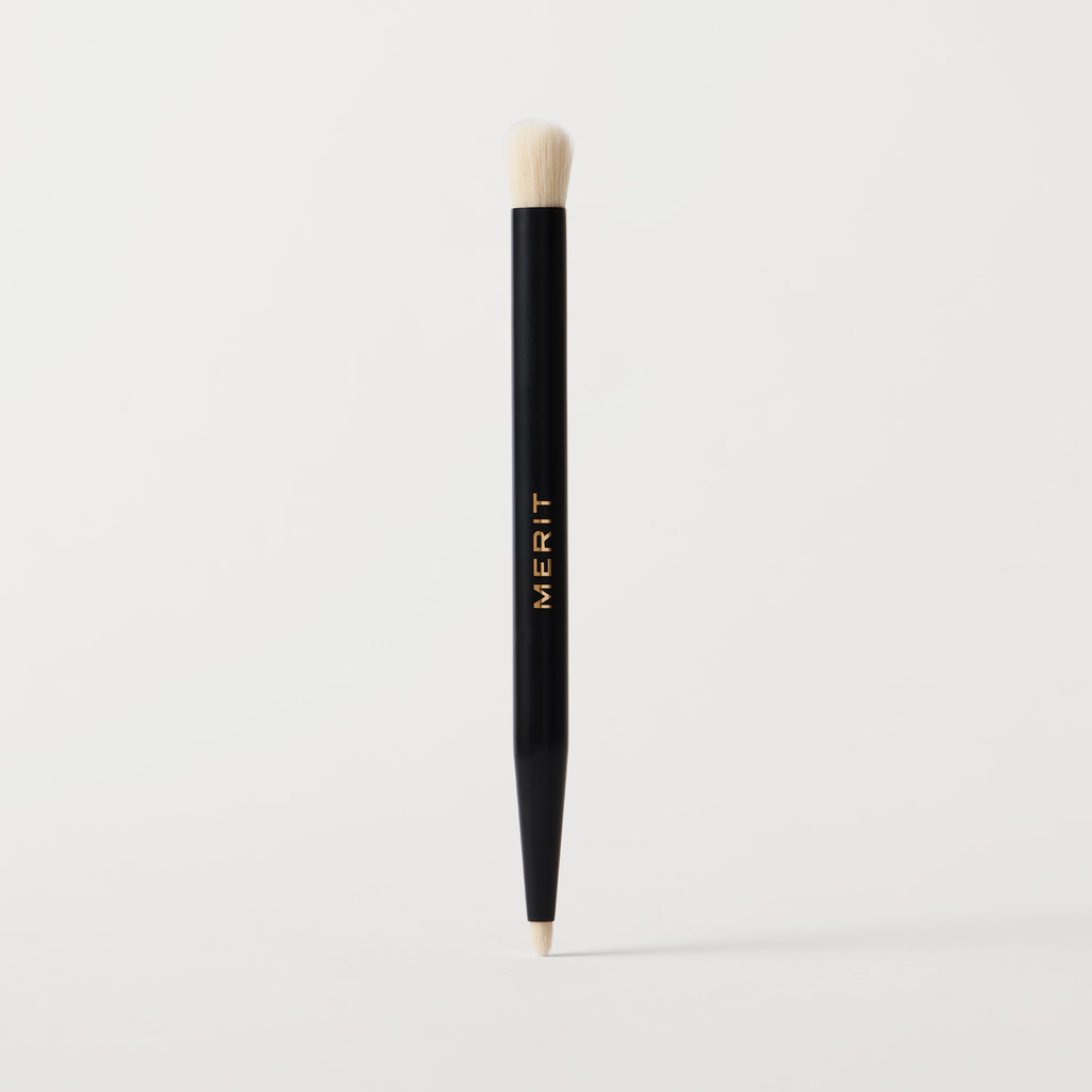 Master || A black cosmetic brush with a flat, dual-ended design, featuring the brand name 'MERIT' in gold lettering on the side.