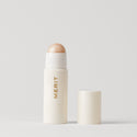 Master || A stick highlighter with the brand name MERIT written on it, with the product cap removed, revealing the highlighter balm in shade Cava