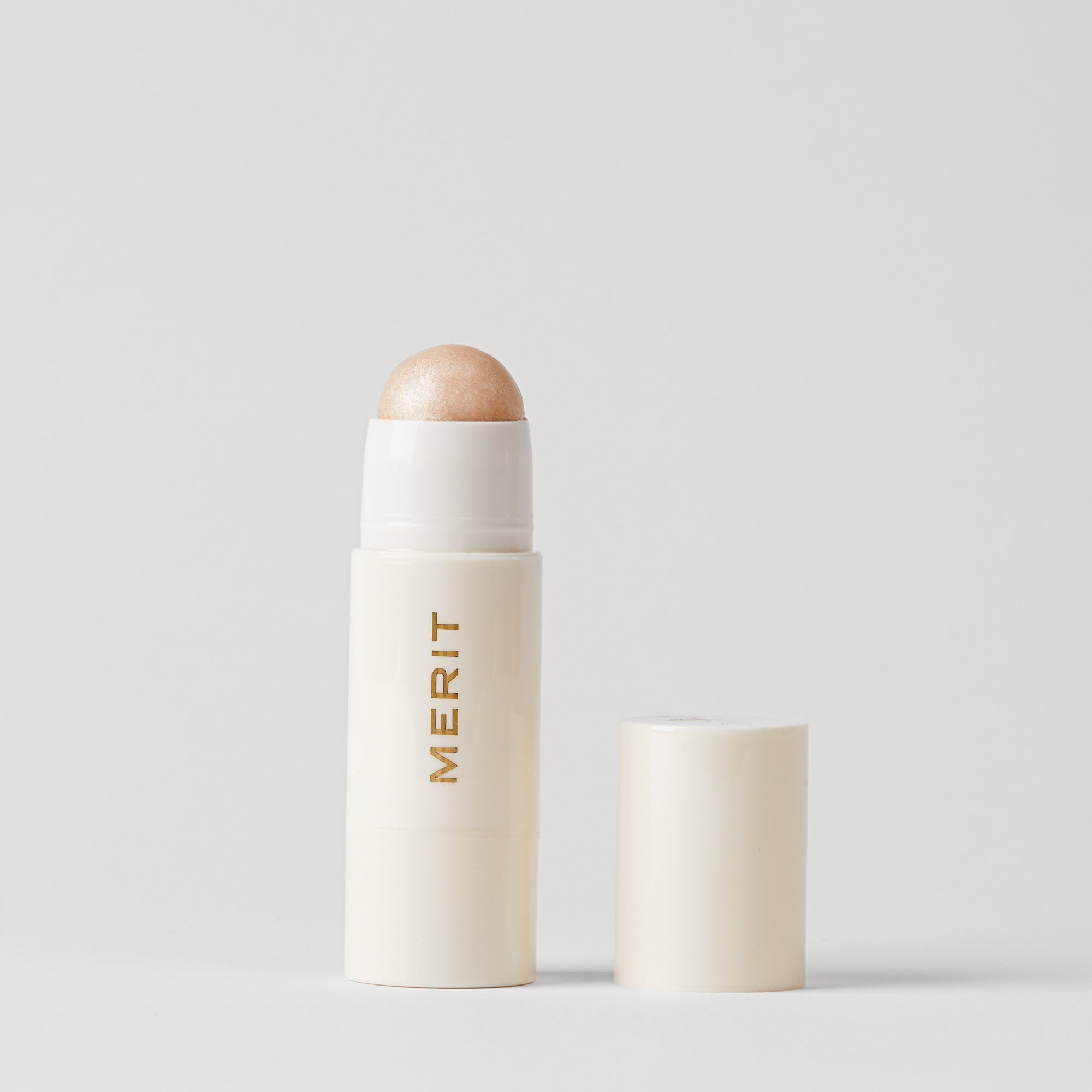Master || A stick highlighter with the brand name MERIT written on it, with the product cap removed, revealing the highlighter balm in shade Cava