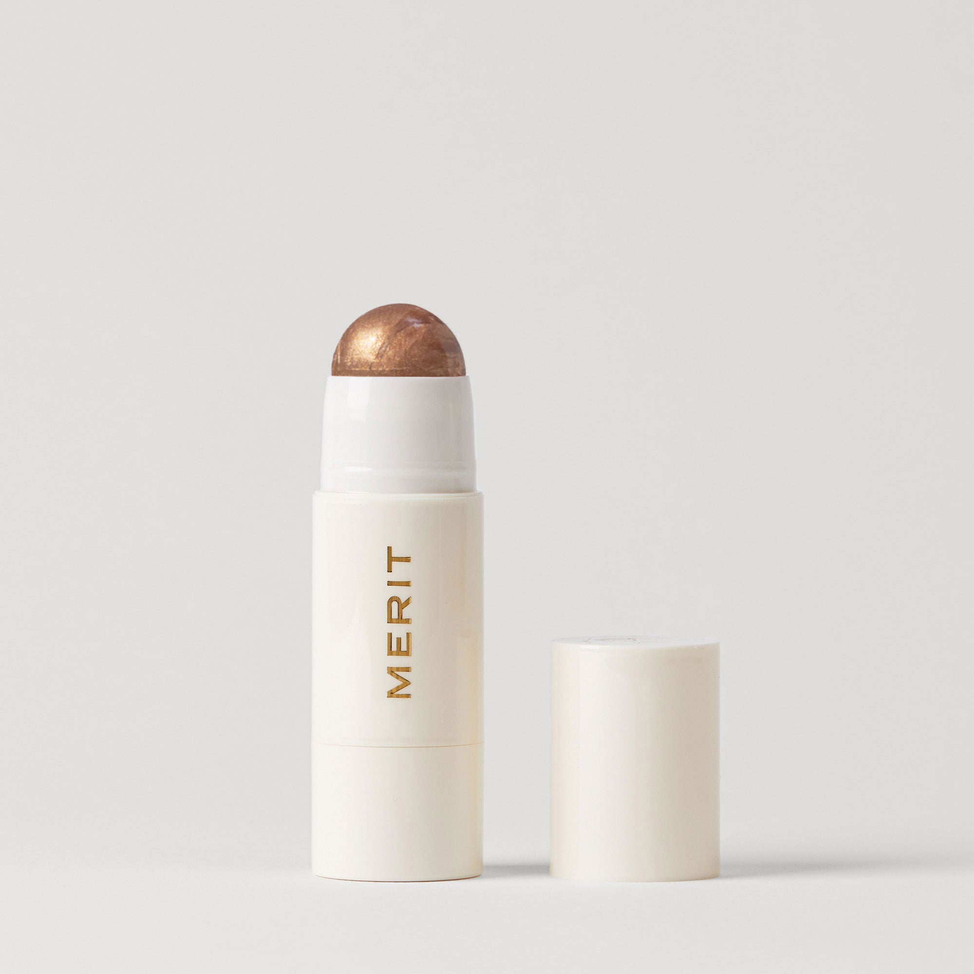 Master || A stick highlighter with the brand name MERIT written on it, with the product cap removed, revealing the highlighter balm in shade Solstice