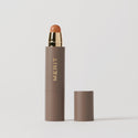 Master || A stick concealer product with the brand name 'MERIT' written on it, with the cap removed, showing the product in shade  Amber 