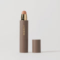 Master || A stick complexion product with MERIT written on it, with the cap removed, showing the product in shade Calico.