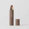 Master || A stick complexion product with MERIT written on it, with the cap removed, showing the product in shade Sepia.