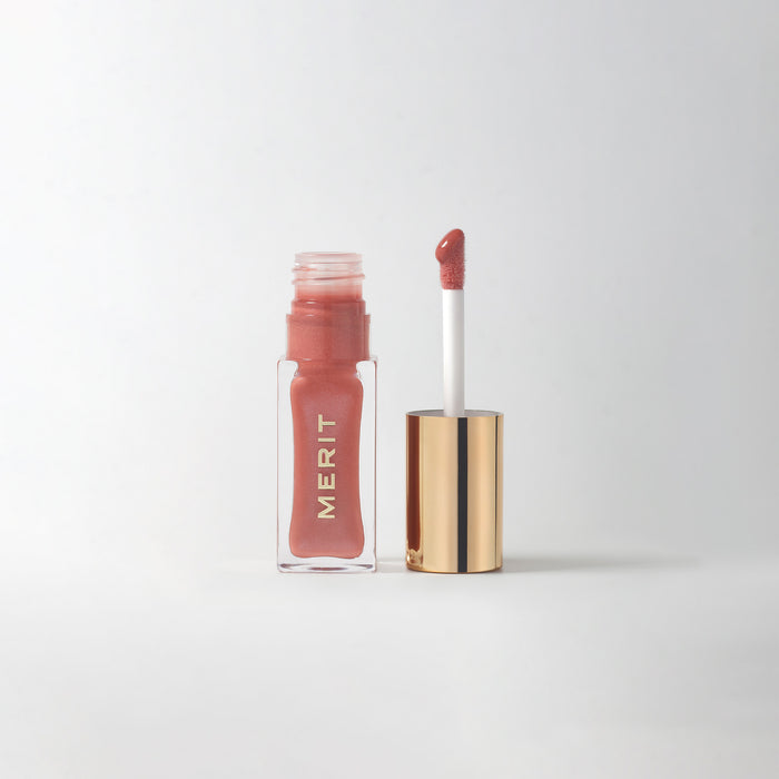 Master || A bottle of Merit lip oil with a pearlescent pink shade displayed next to its applicator.