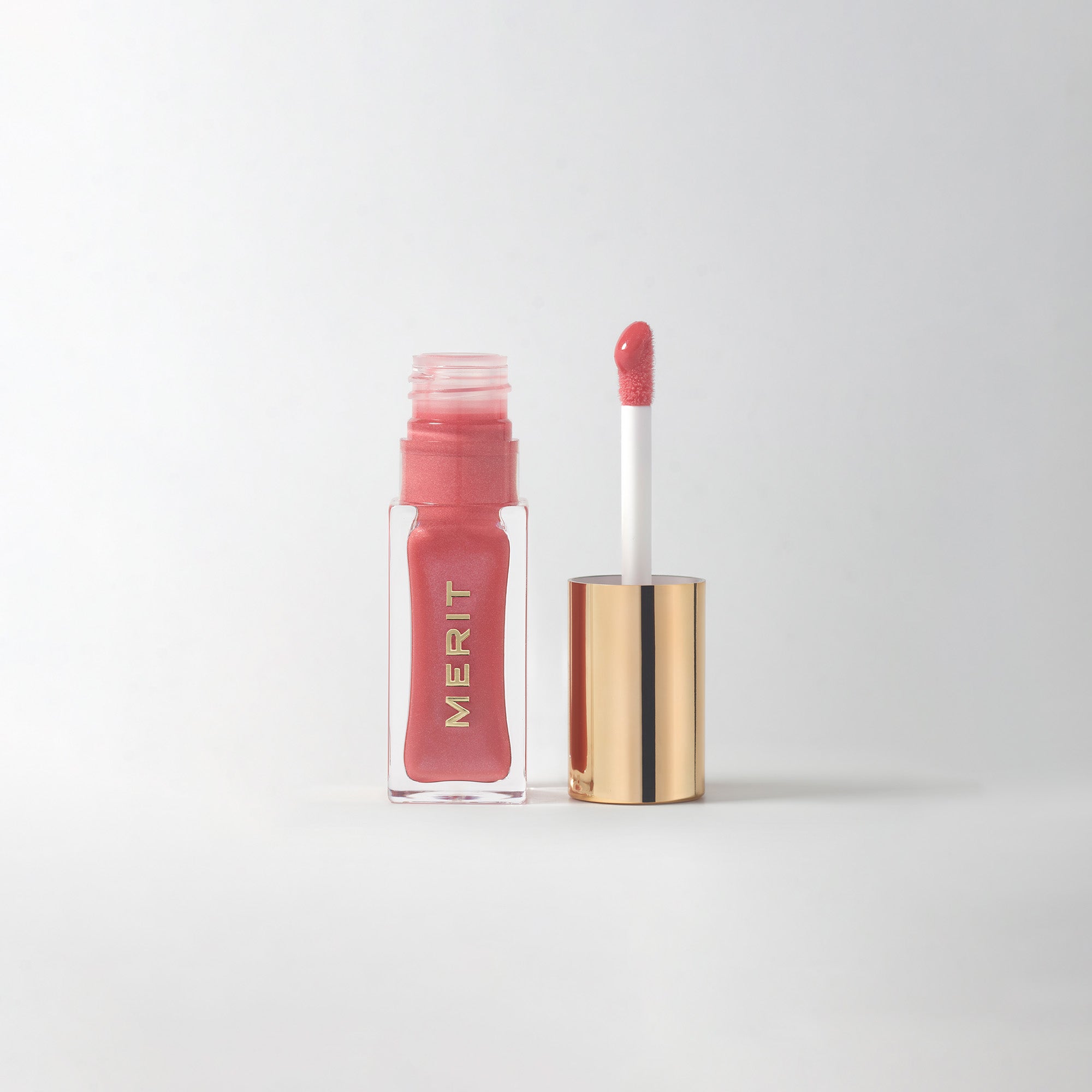Master ||  A bottle of Merit lip oil with a pearlescent pink shade displayed next to its applicator.