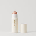 Master || A stick highlighter with the brand name MERIT written on it, with the product cap removed, revealing the highlighter balm 