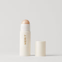 Master ||  A stick highlighter with the brand name MERIT written on it, with the product cap removed, revealing the highlighter balm