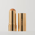 Master ||  A stick bronzer product by MERIT, with the cap off, showing the bronzing cream inside and the brand's name on the cap.